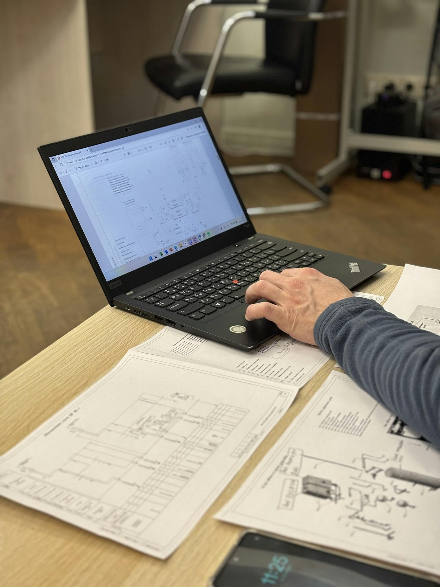 An engineer works on a laptop reviewing technical blueprints and diagrams in an office.